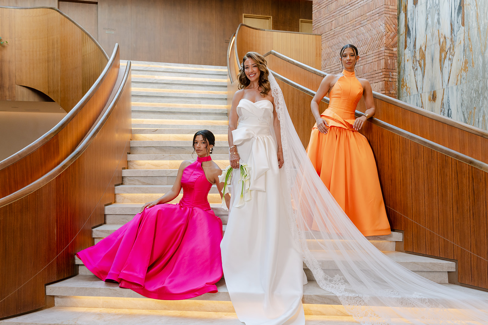 Bride with cathedral lace veil flanked by bridesmaids in fuchsia and orange gowns on the St. Regis Cap Cana staircase